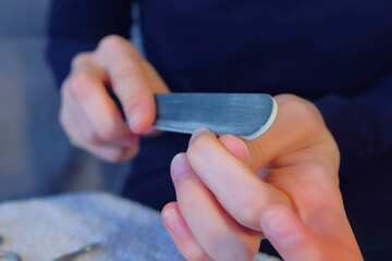 Woman polishes her nails with nail file after remove shellac making oval shape, hands closeup. Making manicure at home for herself. Hygiene and care about nails. Beauty procedure. Tools on table.