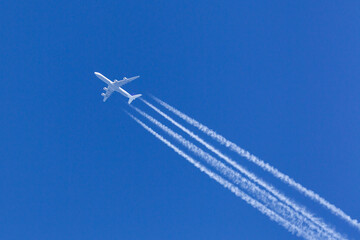 Large four engined commercial airliner jet aircraft flying at high altitude with a large contrail flowing behind it.