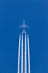 Obraz premium Large four engined commercial airliner jet aircraft flying at high altitude with a large contrail flowing behind it.