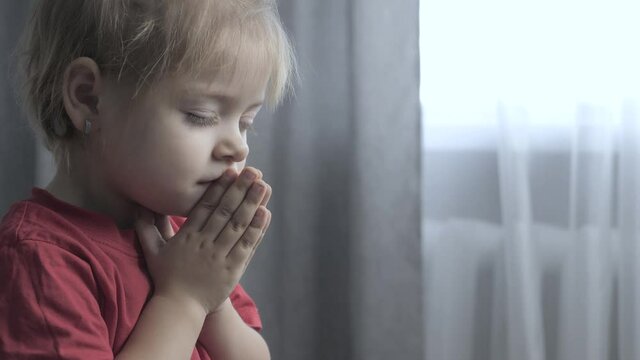 little daughter girl makes a wish prayers bedtime lifestyle religion concept . prayer child indoors praying by bed in front of window