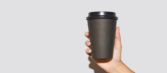 Girl hand hold coffee plastic cup. Grey background with copyspace. Female arm holding paper glass. To go, away. No ecology. Hard shadows. Horizontal banner
