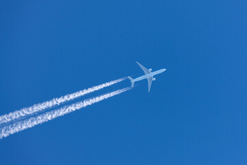 Large twin engined commercial airliner jet aircraft flying at high altitude with a large contrail flowing behind it.