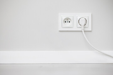 Electrical socket isolated on gray wall. White wire plug plugged in. Renovated studio apartment...