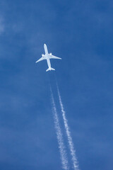 Large twin engined commercial airliner jet aircraft flying at high altitude with a large contrail flowing behind it.