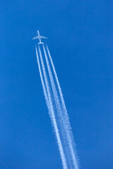 Large four engined commercial airliner jet aircraft flying at high altitude with a large contrail flowing behind it.
