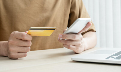 The businessman's hand is holding a credit card and using a smartphone for online shopping and internet payment in the office
