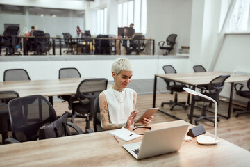 Digital technologies at work. Young, beautiful tattooed business lady in eyewear using digital...