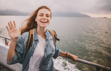 Happy curly young woman traveler on a ship at the sea against the backdrop of a beautiful landscape. Windy weather and flying hair, adventure travel concept