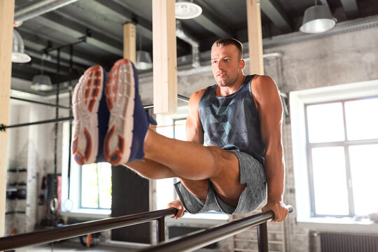 fitness, sport, bodybuilding and people concept - young man doing abdominal exercise on parallel bars in gym