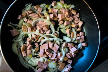 fried pieces of sausages and onion on frying pan