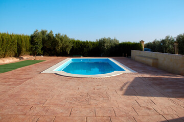 Piscina sobre hormigón rojizo, tonos azulados y verdes.
