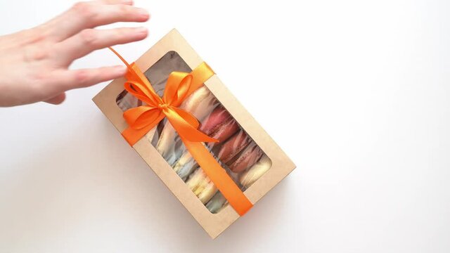 several times box with ribbon and inside macarons enters frame on white table.