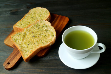 Garlic Butter Toasts on Breadboard with a Cup of Hot Green Tea Served on Black Wooden Table