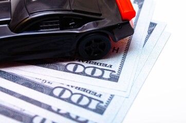 Black toy car on a heap of dollar bills on a white and black background. A sports car with a red...