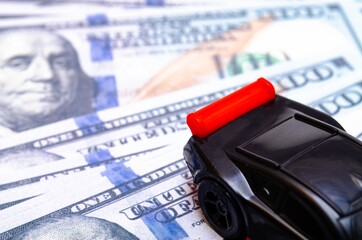 Black toy car on a heap of dollar bills on a white and black background. A sports car with a red...