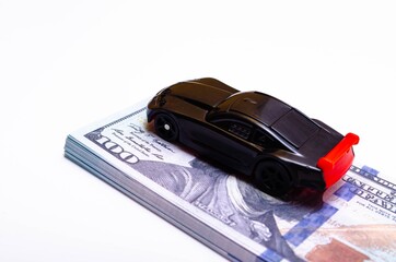 A toy sports car in black with a red wing on a springboard, a podium made of dollar bills. Car and...