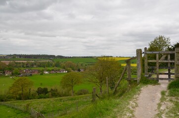 Fototapeta na wymiar Wooden gate on path with panoramic views of countryside in Salisbury, England. Views of green and yellow fields and villages