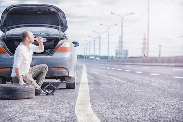 Replacing the wheel of a car on the road. A man doing tire work on the sidelines.