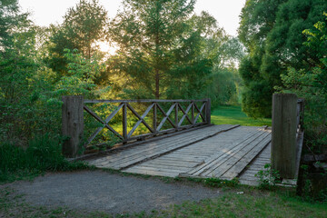 Landscape photo of a wooden bridge with trees on either side. The sun is setting. 