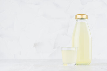 Fresh yellow pineapple juice in glass bottle mock up with wine glass on white wood table in light interior, template for packaging, advertising, design, branding product.
