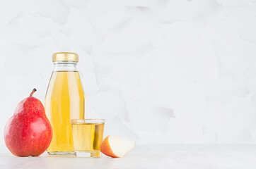 Bright yellow transperent pear juice in glass bottle mock up with wine glass, fruit slice on white wood table in light interior, template for packaging, advertising, design, branding product.