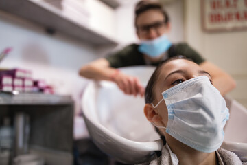 Hairdresser and girl child customer in a salon with medical masks during virus pandemic. Working with safety mask.