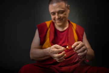 Buddhist monk in red kesa, holding an incense stick with incense in his hand