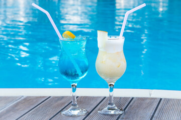 Two summer sweet cocktails by the pool. Blue lagoon and Pina colada in a glass with a straw. Mixed alcoholic drink. Beach party concept.