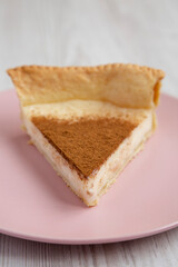 Homemade Sugar Cream Pie on a pink plate on a white wooden background, low angle view. Close-up.