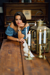 beautiful girl is leaning on wooden table on which there are candles.