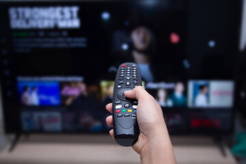 Close-up of hands using remote smart tv on blurred smart tv with video on demand as background