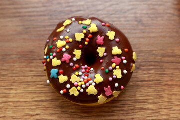 Single brown donut on a wood background. Chocolate glazed donut. Rainbow dots decoration