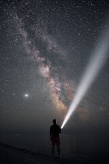 Fototapeta na wymiar traveller and galaxy. milky way astrophoto. man stands on the sea shore with flash light. light beam and man during night.
