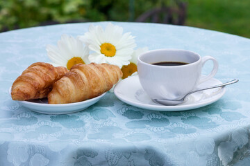 Obraz na płótnie Canvas On the table with a tablecloth is a cup of fresh black coffee with a delicious creamy croissant.