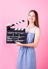 Happy smiling teenager girl in a blue dress holding a clapper board isolated on pink