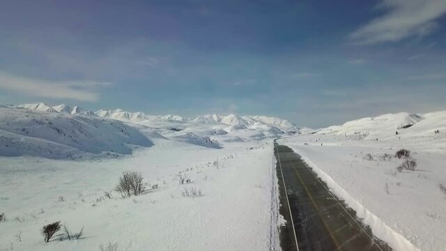 Spectacular white winter snow scene descending on Yukon Haines highway, route of old Dalton Trail with mountain range in background on colorful blue sunny sky day, Alaska, overhead aerial down