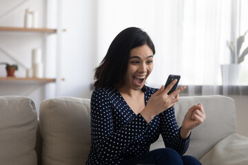 Overjoyed millennial Asian girl look at cellphone screen feel euphoric get unexpected good message or text, excited young Vietnamese woman triumph read unbelievable news on smartphone gadget