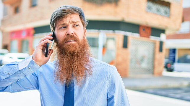 Young handsome redhead businessman smiling happy. Standing with smile on face having conversation talking on the smartphone at street of city.