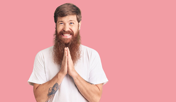 Handsome Young Red Head Man With Long Beard Wearing Casual White Tshirt Praying With Hands Together Asking For Forgiveness Smiling Confident.