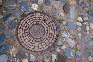 A manhole cover on an old cobblestone pavement