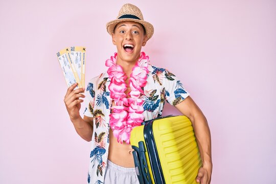 Young hispanic boy wearing summer style holding cabin suitcase and boarding tickets celebrating crazy and amazed for success with open eyes screaming excited.