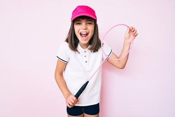 Young little girl with bang holding badminton racket smiling and laughing hard out loud because funny crazy joke.