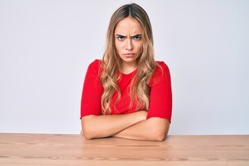 Young beautiful blonde woman wearing casual clothes sitting on the table skeptic and nervous, disapproving expression on face with crossed arms. negative person.