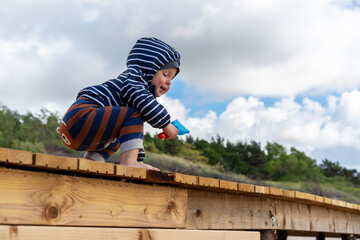 Cheerful baby boy playing on wooden path in the sandy Baltic sea beach. Post Quarantine family vacation in native resort.