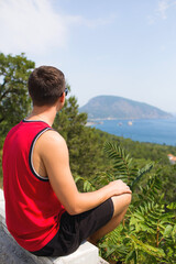 Fototapeta premium Happy man traveler sitting on mountain alone and looking at the sea. Photos for ads and billboards.