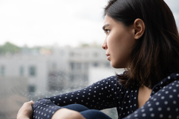 Sad Asian millennial girl look in window distance thinking or pondering alone at home, thoughtful...