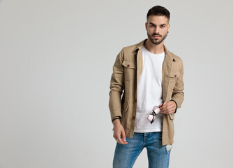 confident young casual man in jacket holding sunglasses