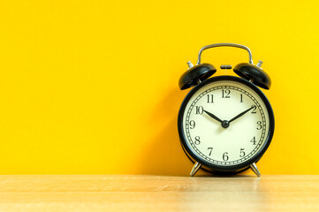 black alarm clock on a yellow background, business concept