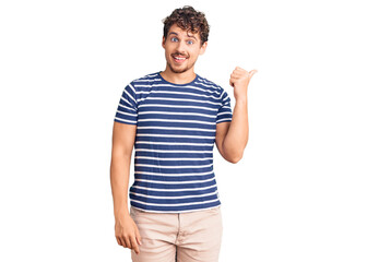 Fototapeta premium Young handsome man with curly hair wearing casual clothes smiling with happy face looking and pointing to the side with thumb up.