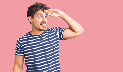 Young handsome man with curly hair wearing casual clothes very happy and smiling looking far away...